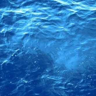 Close-up view of ocean water with rippling waves and sunlight reflections, representing climate impacts on marine ecosystems and water resources