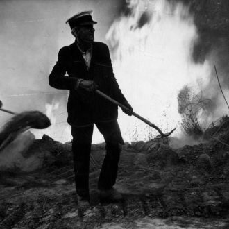 Wildfire Response with Hand Tools – Climate Resolve Historic black-and-white image of a person using a shovel to control a wildfire, with flames and smoke in the background, reflecting Climate Resolve’s focus on fire resilience